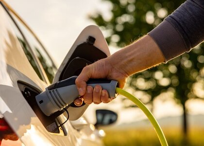 Hand of man inserting a power cord into an electric car for charging ecofriendly vehicle on green landscape Image showing the arm of a man plugging in a charger into an electric car.