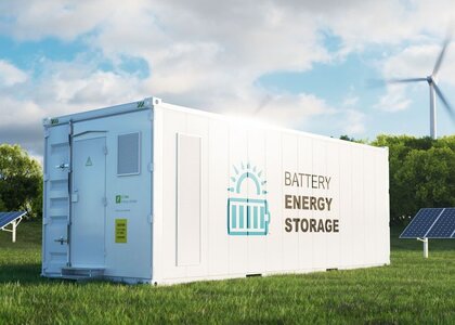 Concept of a modern high-capacity battery energy storage system in a container with a forest in the background Image showing a modern high-capacity battery energy storage systemIn a green field with solar panels in the background sits a large white container with the words “Batter energy storage” written on the side.