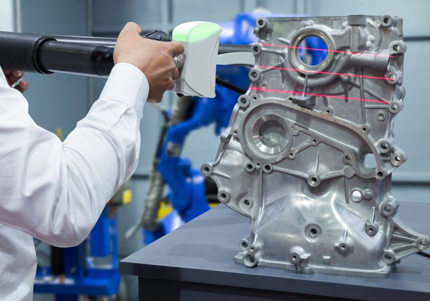 Image showing an engineer working with a portable measuring instrument.To the right of the image an aluminium automotive part sits on a bench being scanned by an engineer with a portable measuring instrument.