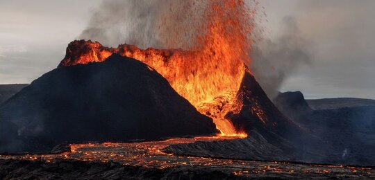 In the foreground is an erupting volcano in Iceland with a lava flow descending its flank