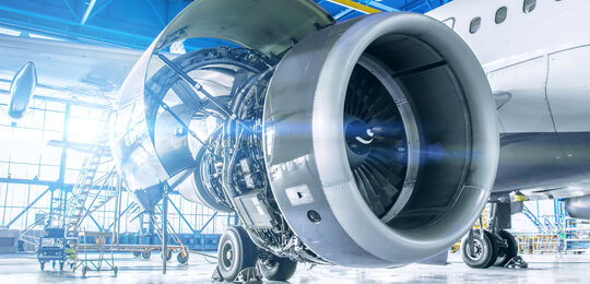 Close up image of maintenance being performed on the exposed engine of an aircraft inside a large hanger