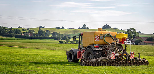 In the early morning light a tractor in the foreground is spraying pesticide over rows of low plants in a large open field