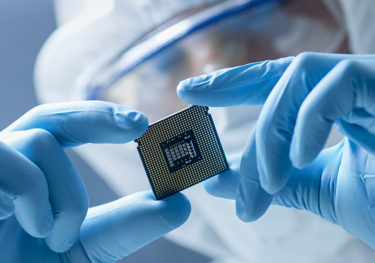 Image showing engineer in sterile coverall holding microchip with gloves and examining it