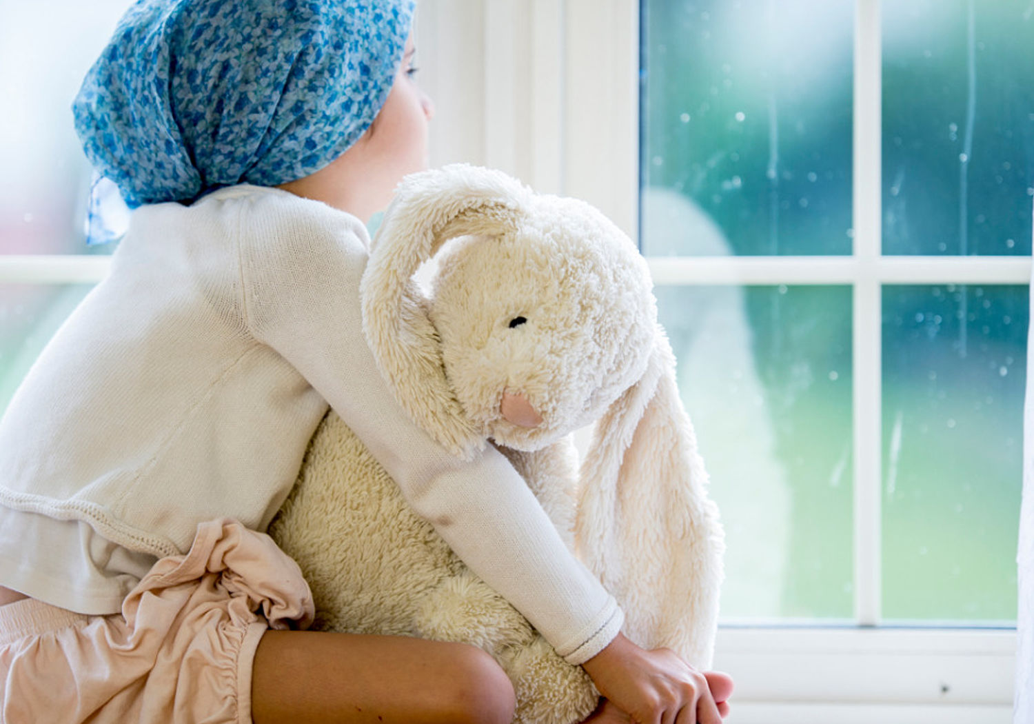 Image of a small child with toy sitting at a windowsill