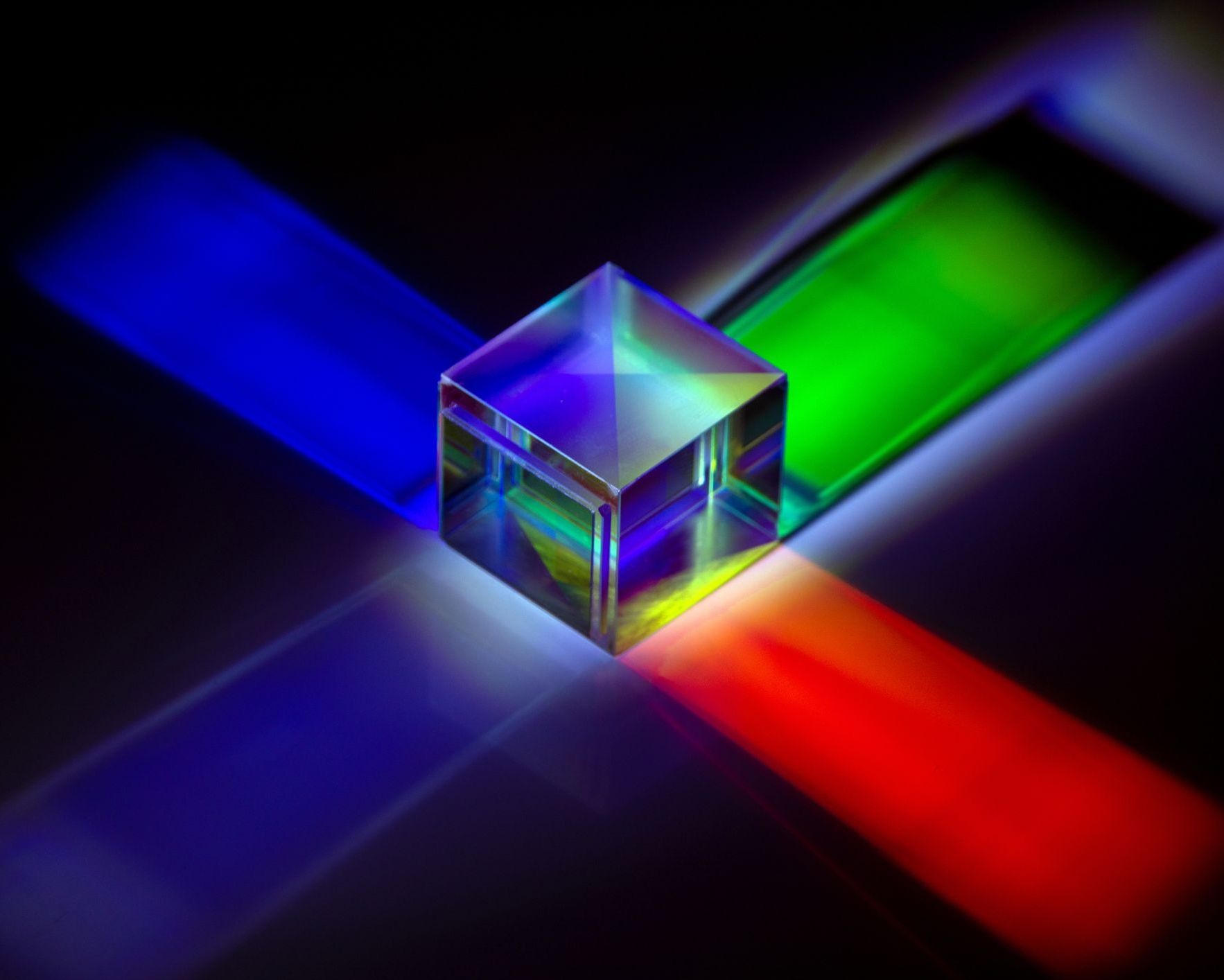 Against a black background a glass cube gives out blue, green and red light from its sides