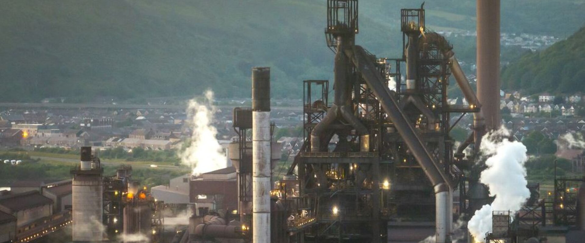 Aerial view of a steel plant in the UK Against a hazy grey sky a large steel plant sits in a valley with white smoke plumes emitted from its large chimney stacks
